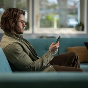 En mann som sitter i en sofa og ser på telefonen sin