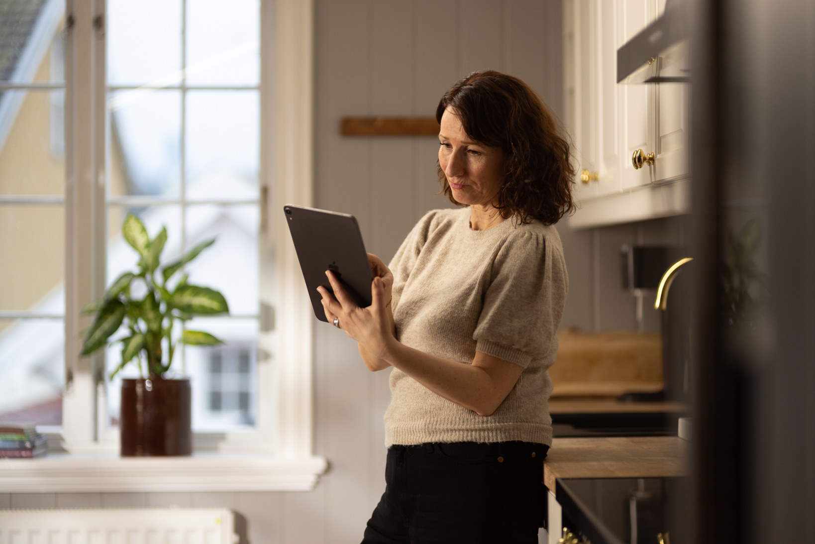 En kvinne som står på et kjøkken med et nettbrett i hendene