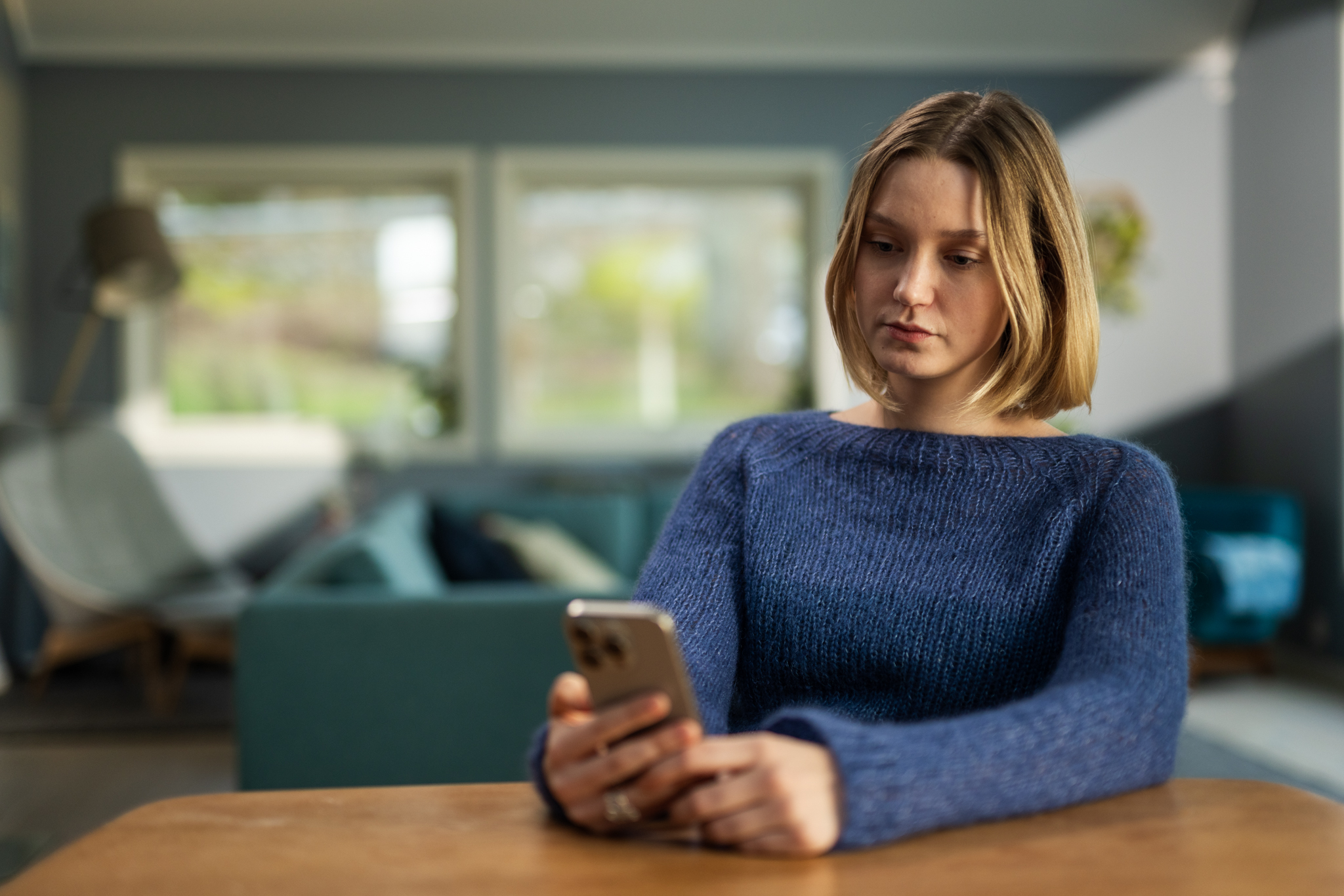 En kvinne som sitter ved et bord og ser på telefonen sin