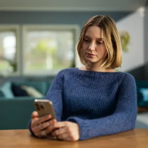 En kvinne som sitter ved et bord og ser på telefonen sin