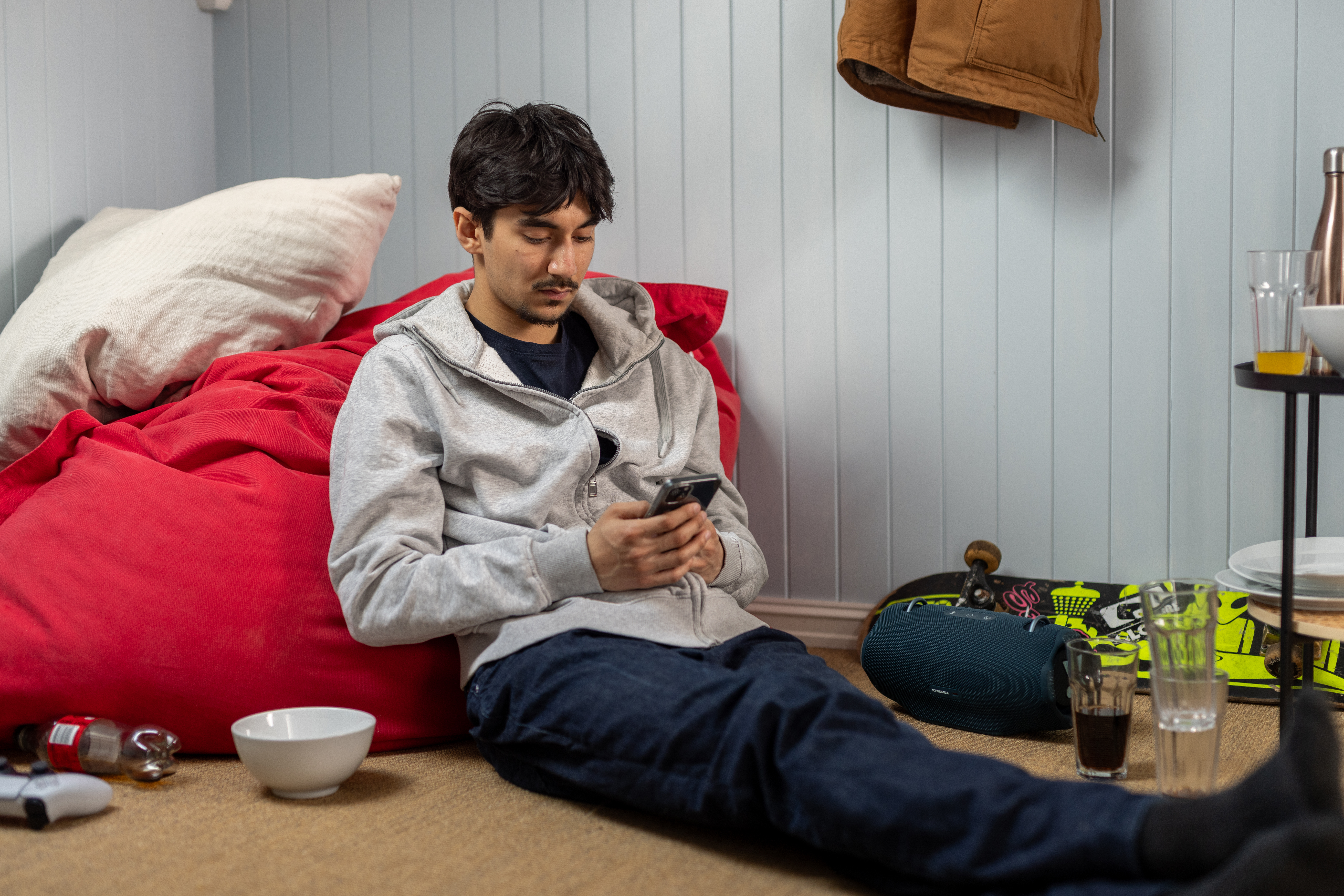 En mann i slutten av tenårene som sitter på gulvet på rommet sitt med mobilen