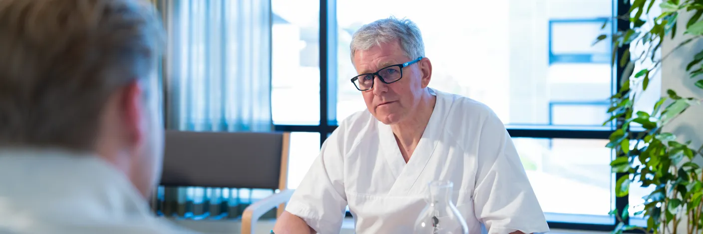 Behandler i hvitt arbeidsantrekk sitter ved et bord